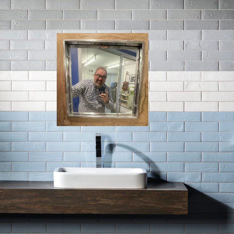 A man is standing in front of a 13000 WALL mirror in a bathroom.
