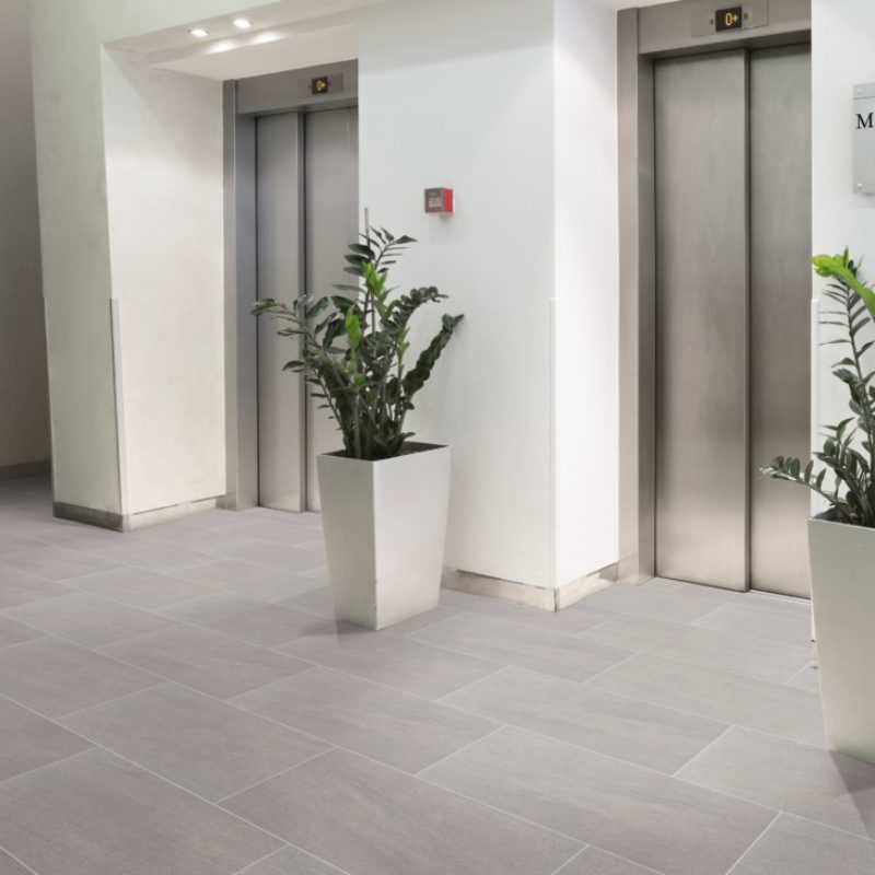 A grey 7000 FLOOR tiled lobby with plants and an elevator.